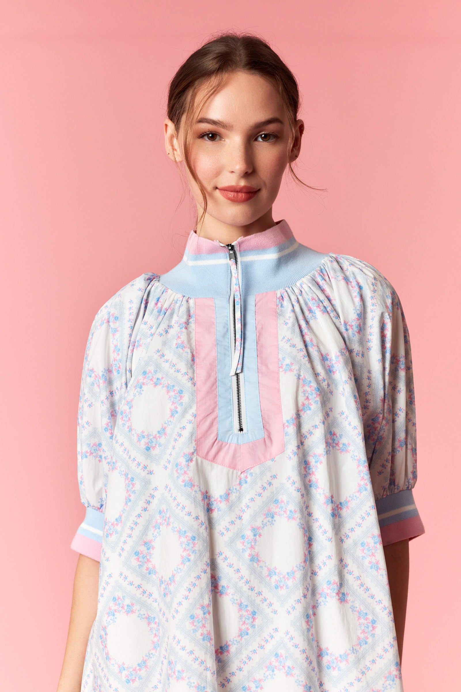 Woman wearing a patterned dress with a pink collar against a pink background