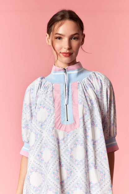 Woman wearing a patterned dress with a pink collar against a pink background