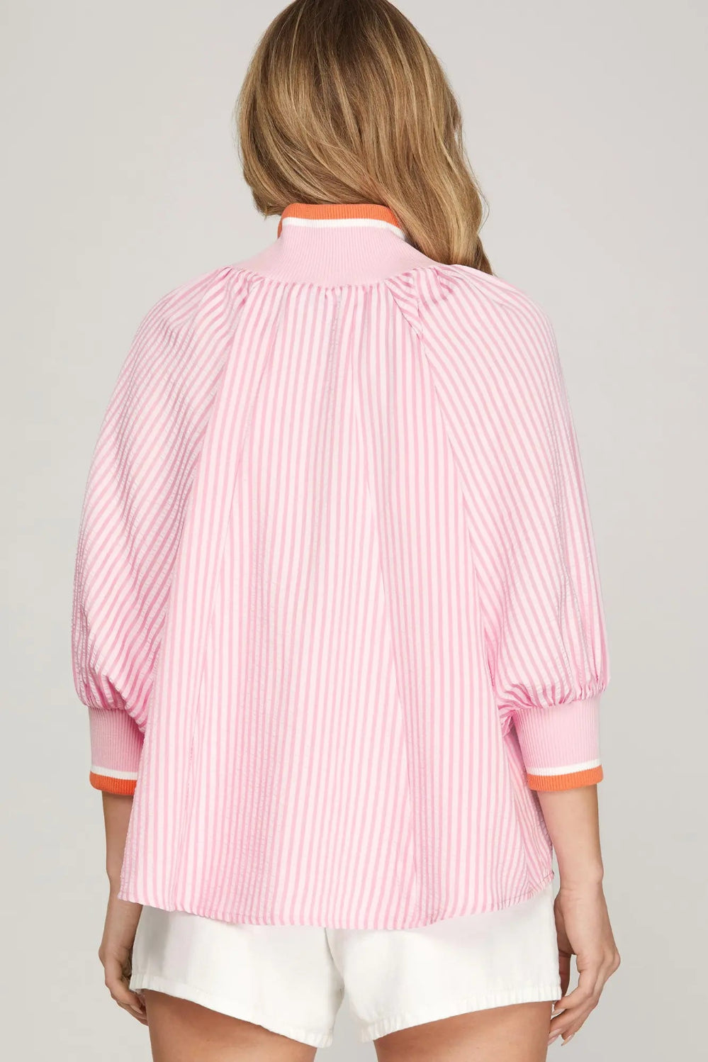 Person wearing a pink striped shirt with orange trim on a plain background