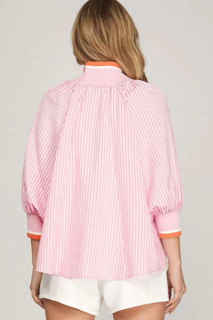 Person wearing a pink striped shirt with orange trim on a plain background