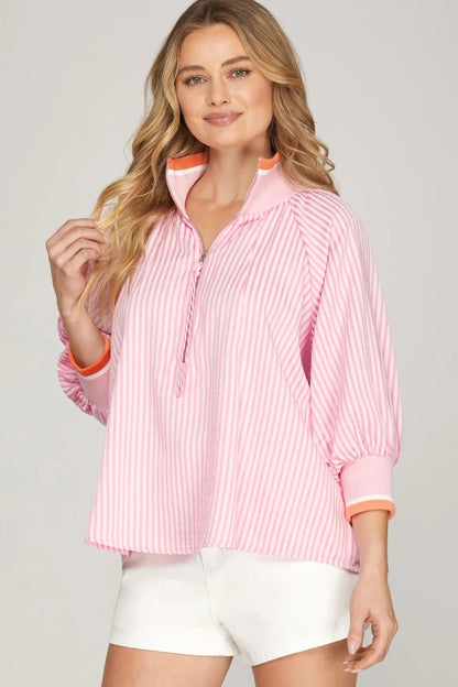 Woman wearing a pink striped shirt with orange trim on a plain background