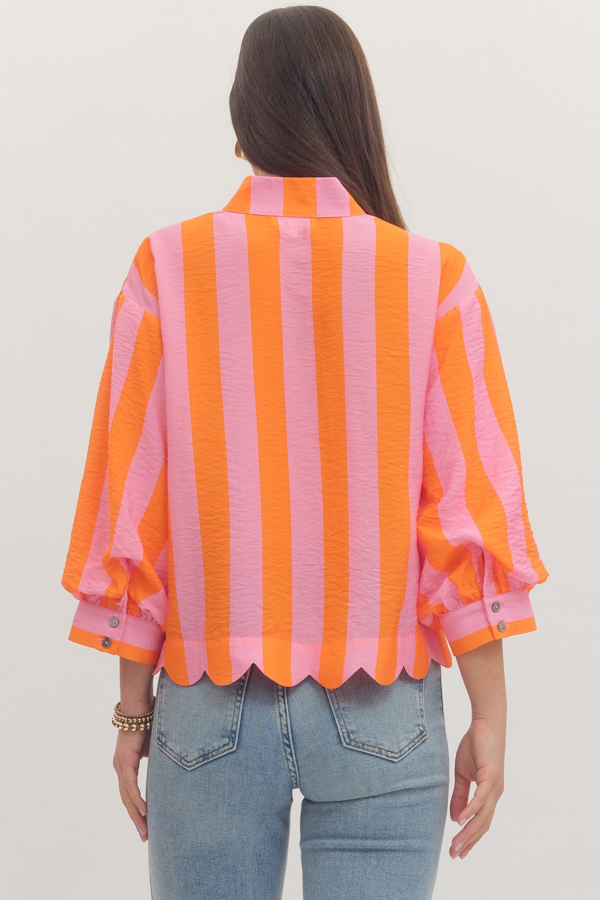 Person wearing a pink and orange striped shirt with blue jeans on a plain background