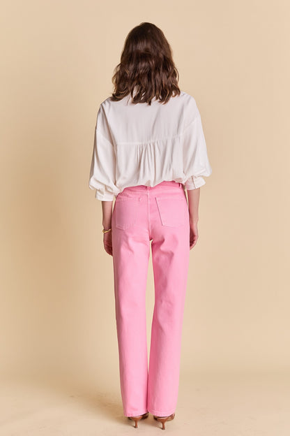 Woman wearing a white blouse and pink pants against a beige background