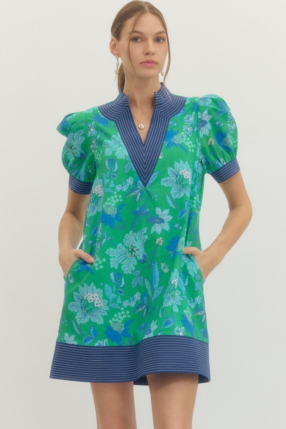 Woman wearing a green floral dress with blue accents on a plain background