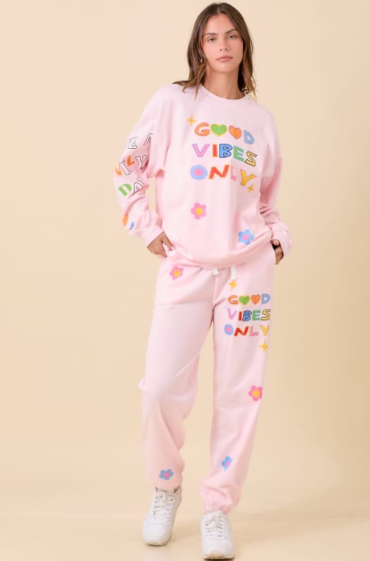 Person wearing a pink 'Good Vibes Only' outfit on a beige background