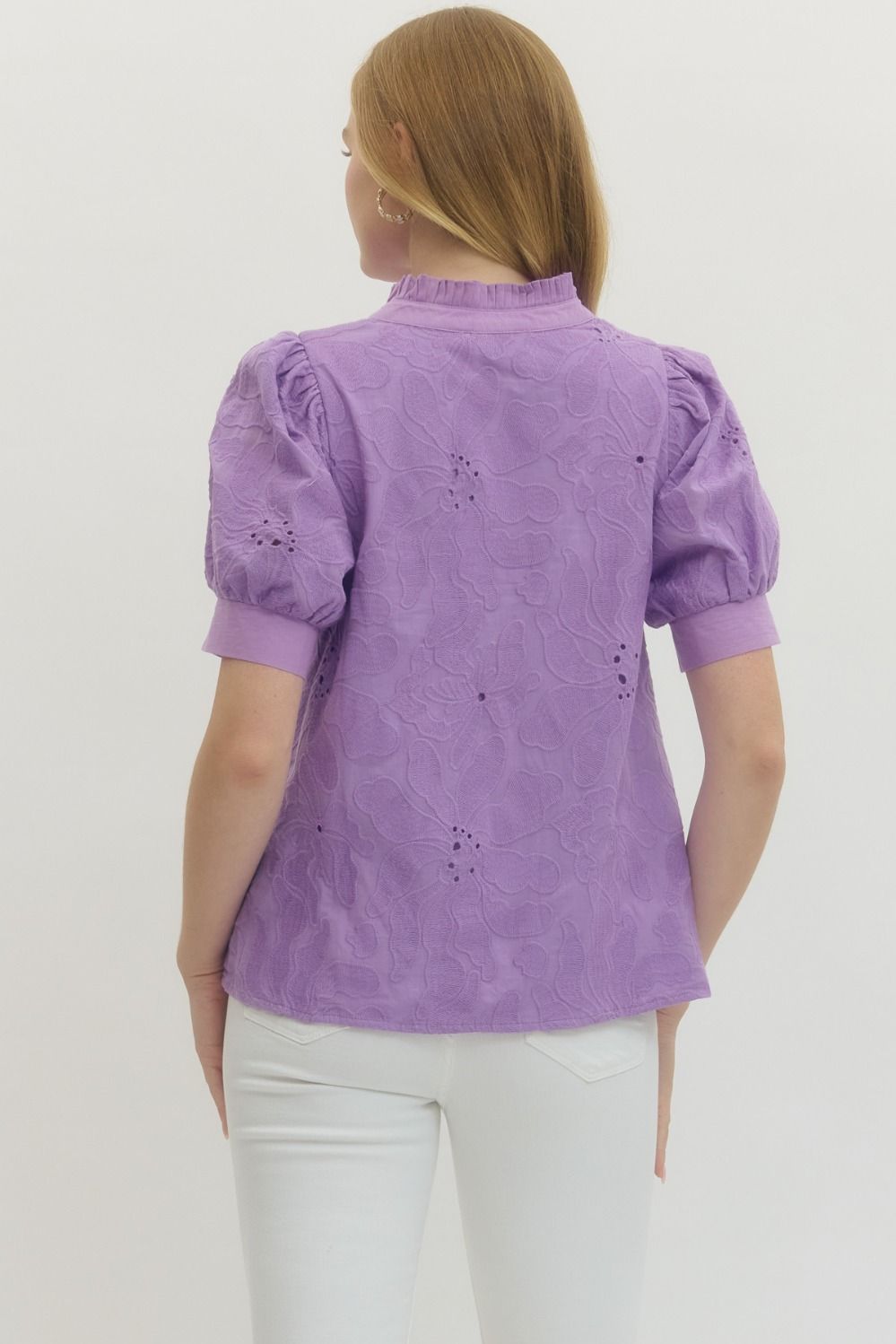 Woman wearing a purple blouse with white pants on a plain background