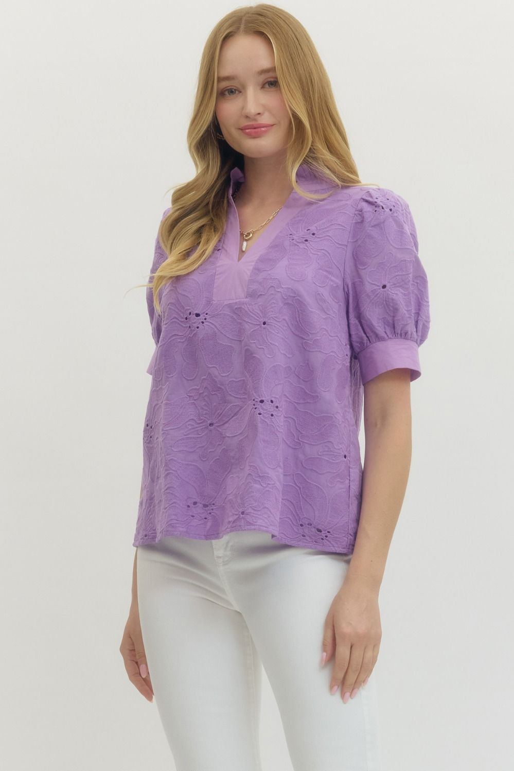 Woman wearing a purple blouse with white pants on a plain background