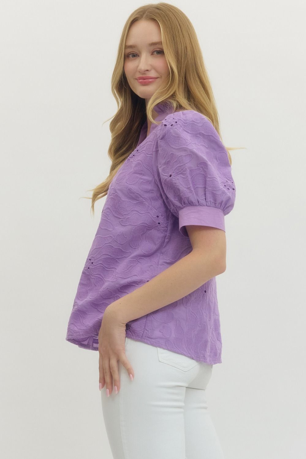 Woman wearing a purple blouse with white pants on a plain background