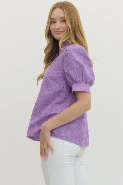Woman wearing a purple blouse with white pants on a plain background
