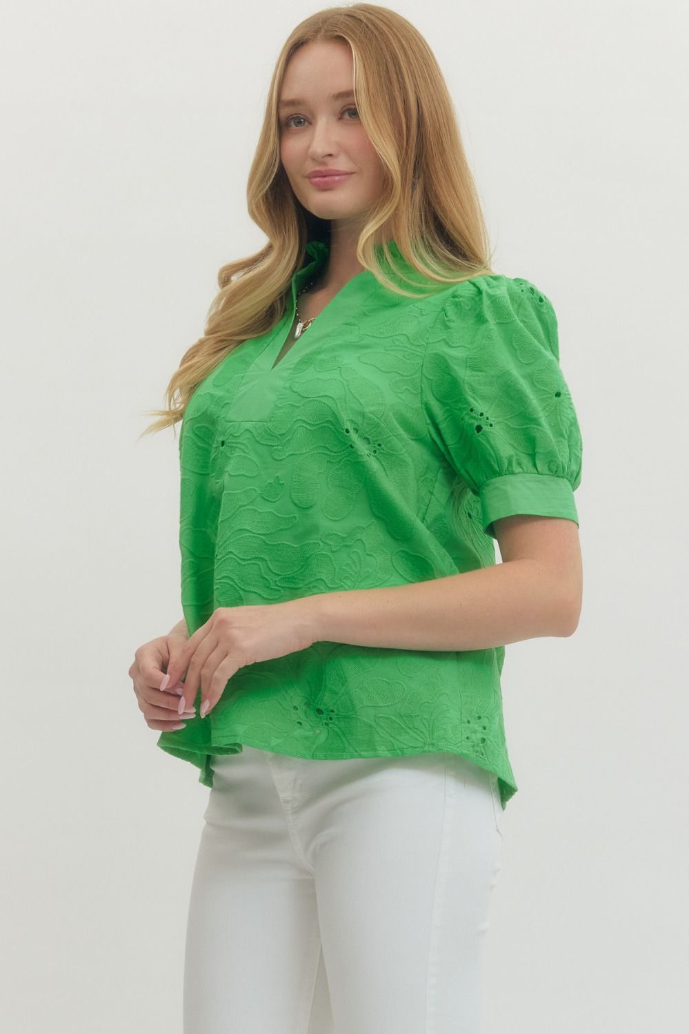 Woman wearing a green blouse with white pants on a plain background