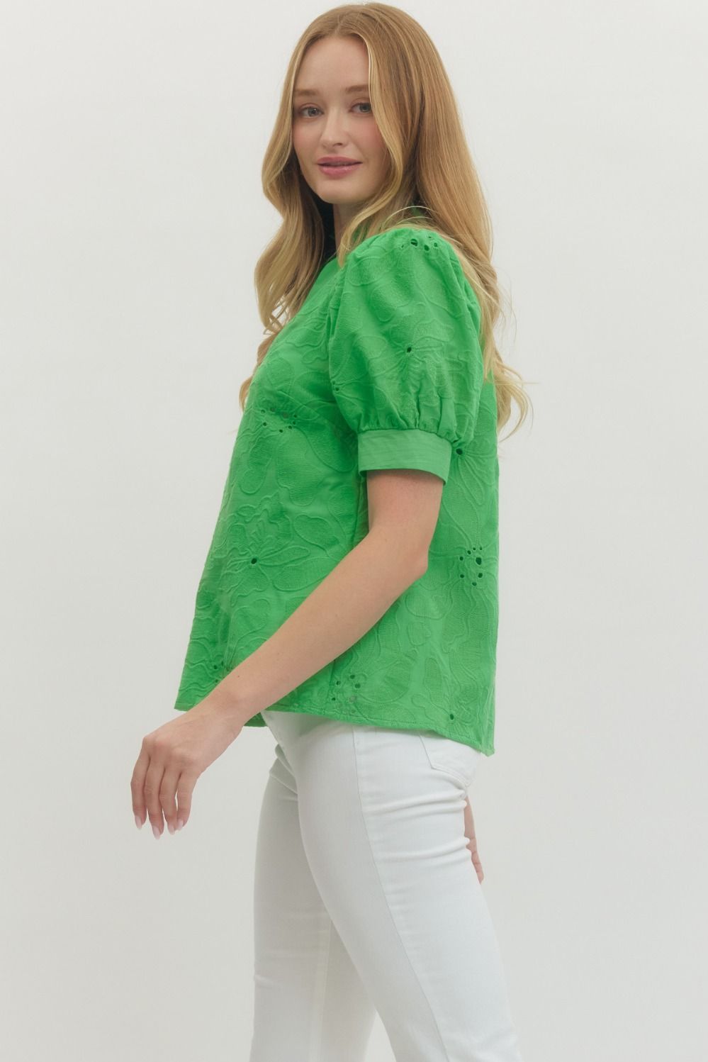 Woman wearing a green blouse with white pants on a plain background