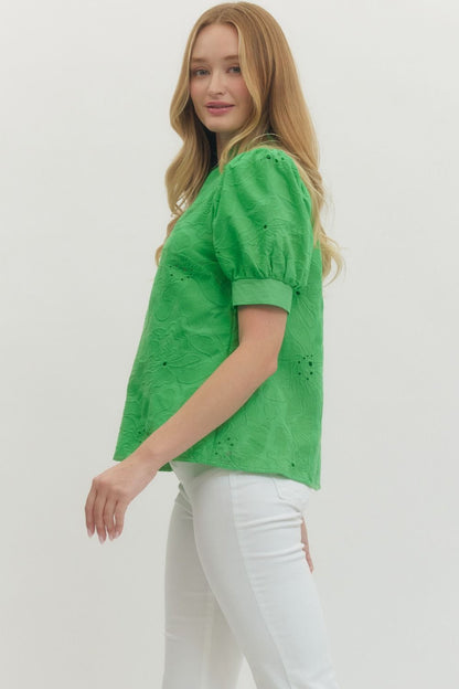 Woman wearing a green blouse with white pants on a plain background