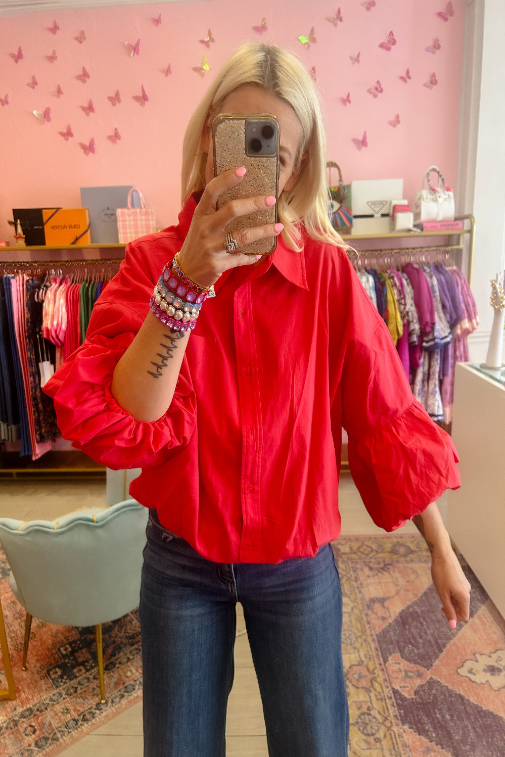 Person wearing a red blouse and blue jeans in a store with pink walls and butterfly decorations.