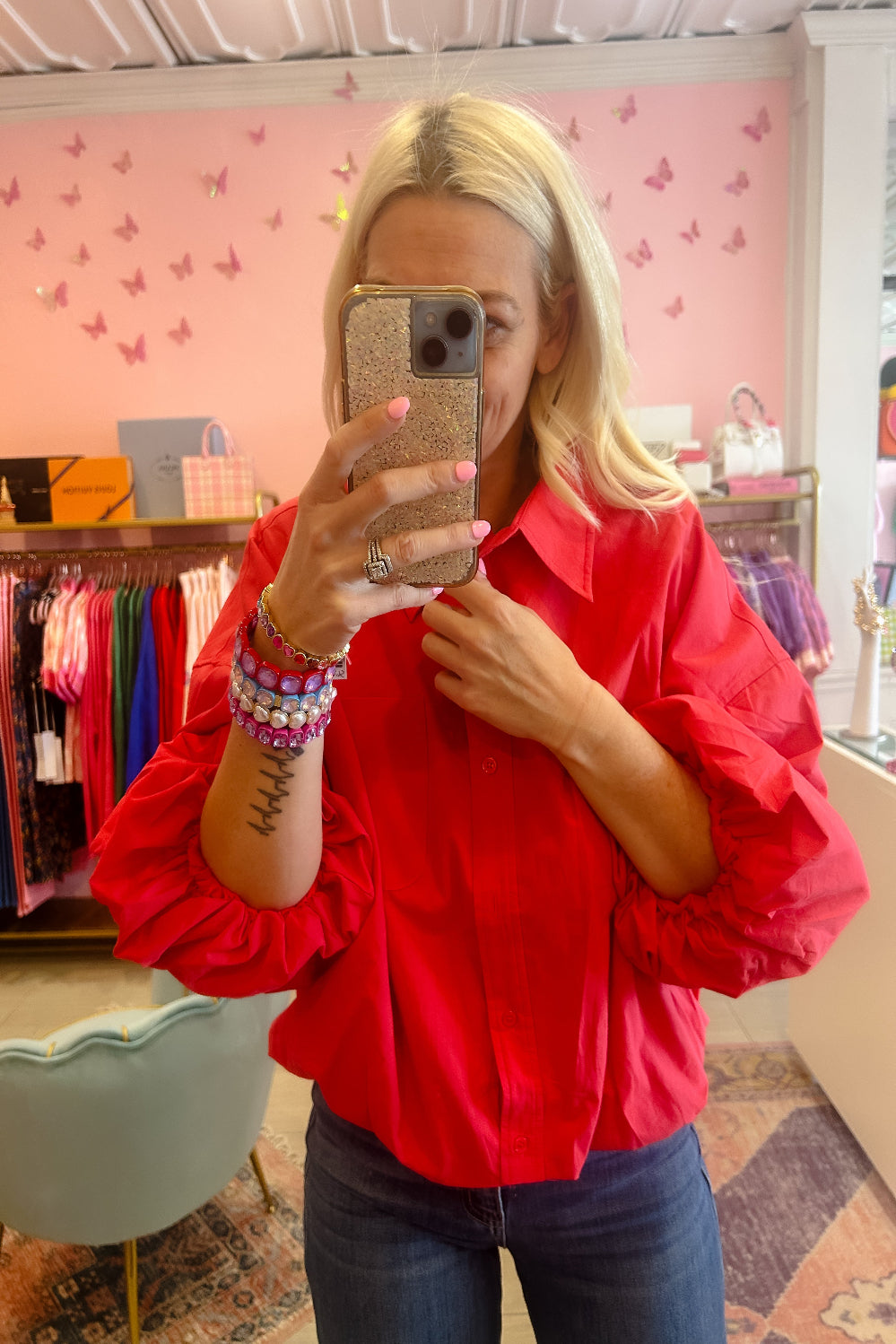 Person wearing a red blouse taking a mirror selfie in a store with pink walls and butterfly decorations.