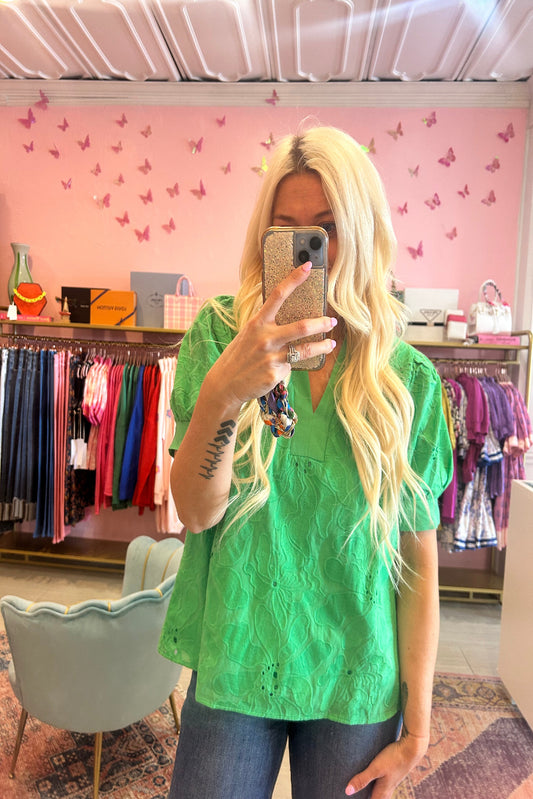 Person wearing a green eyelet top with long blonde hair in a store setting.
