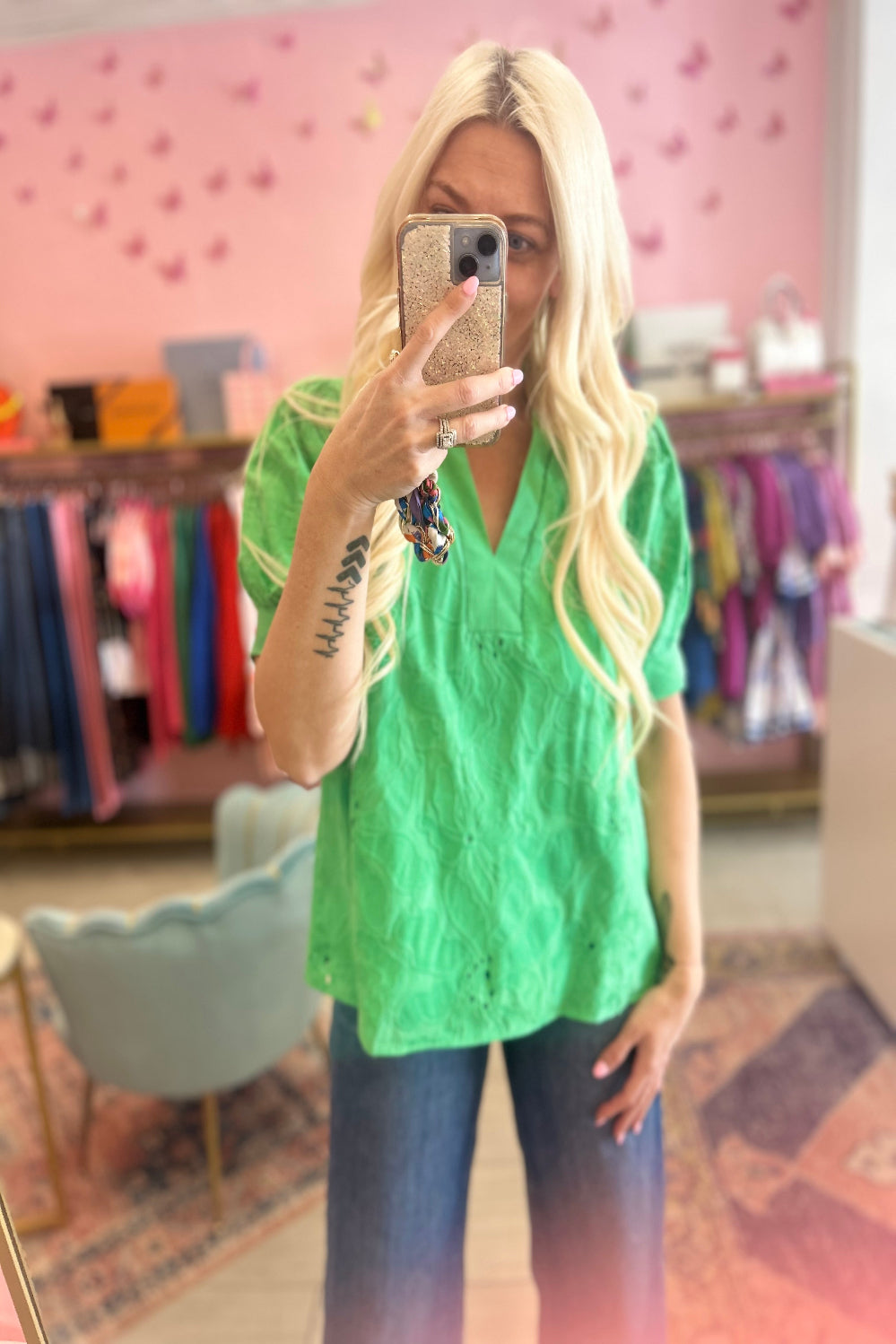 Person wearing a green top and blue jeans taking a mirror selfie in a store.