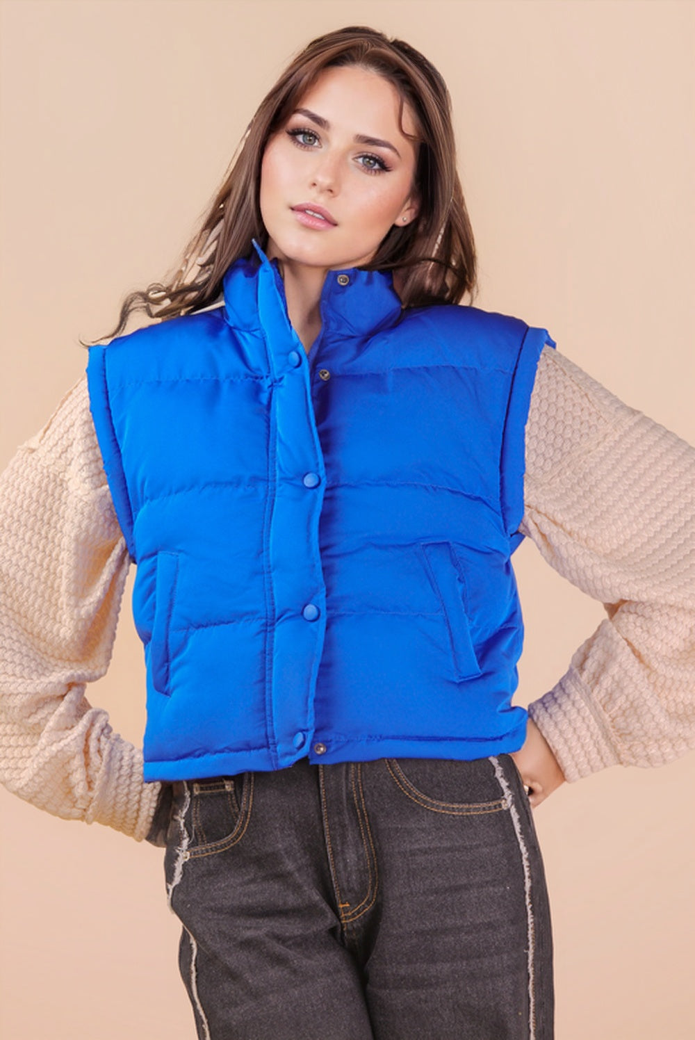 A woman wearing a bright Thunder Blue puffer vest styled over a textured long-sleeve top and dark denim jeans.