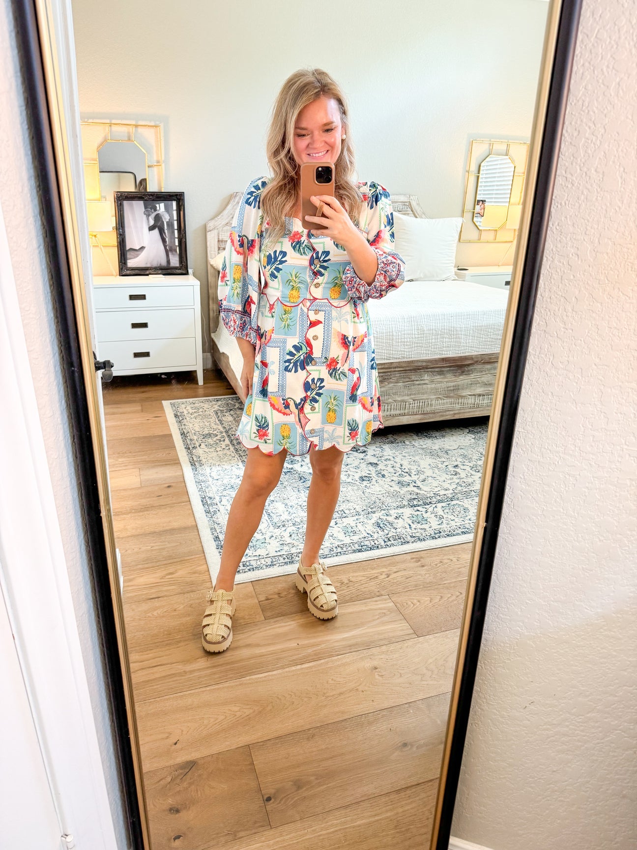 Woman taking a mirror selfie wearing a floral dress in a bedroom.