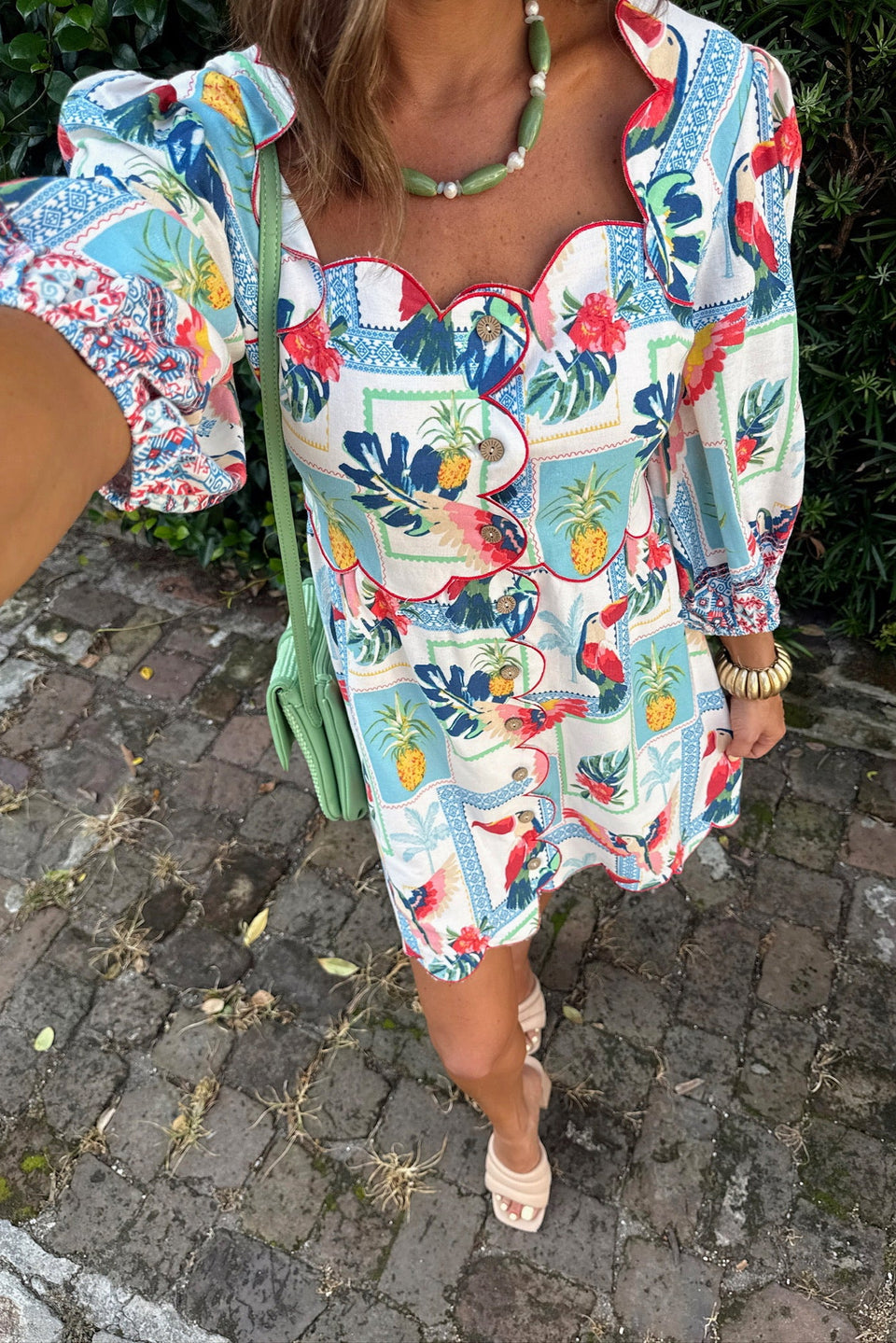 Person wearing a colorful floral dress with pineapple pattern on a cobblestone street.