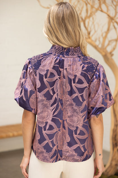 Back view of The Twilight Bloom Top highlighting smocked shoulders and blush floral print on violet satin fabric