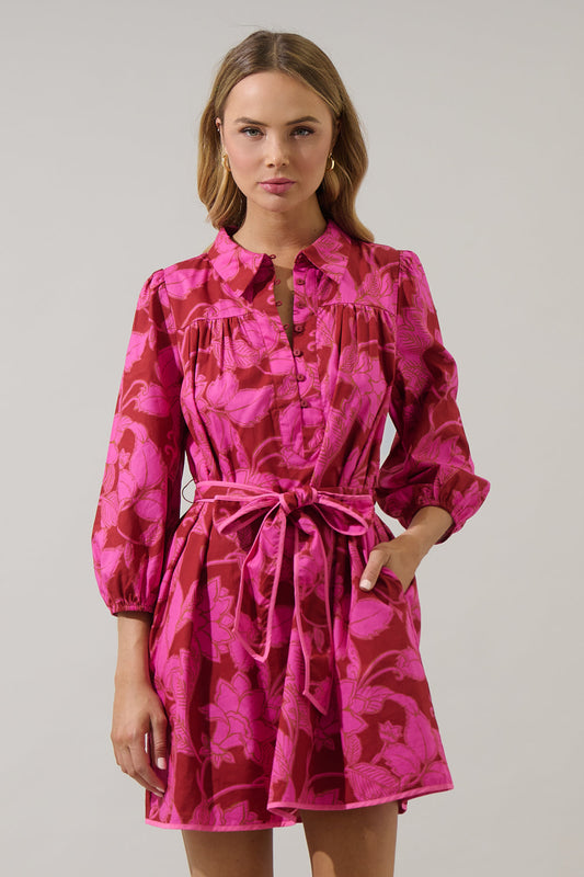 Model wearing a bright pink and magenta floral mini dress with a collared neckline, button front, and waist tie belt from Milo & Lily Boutique.