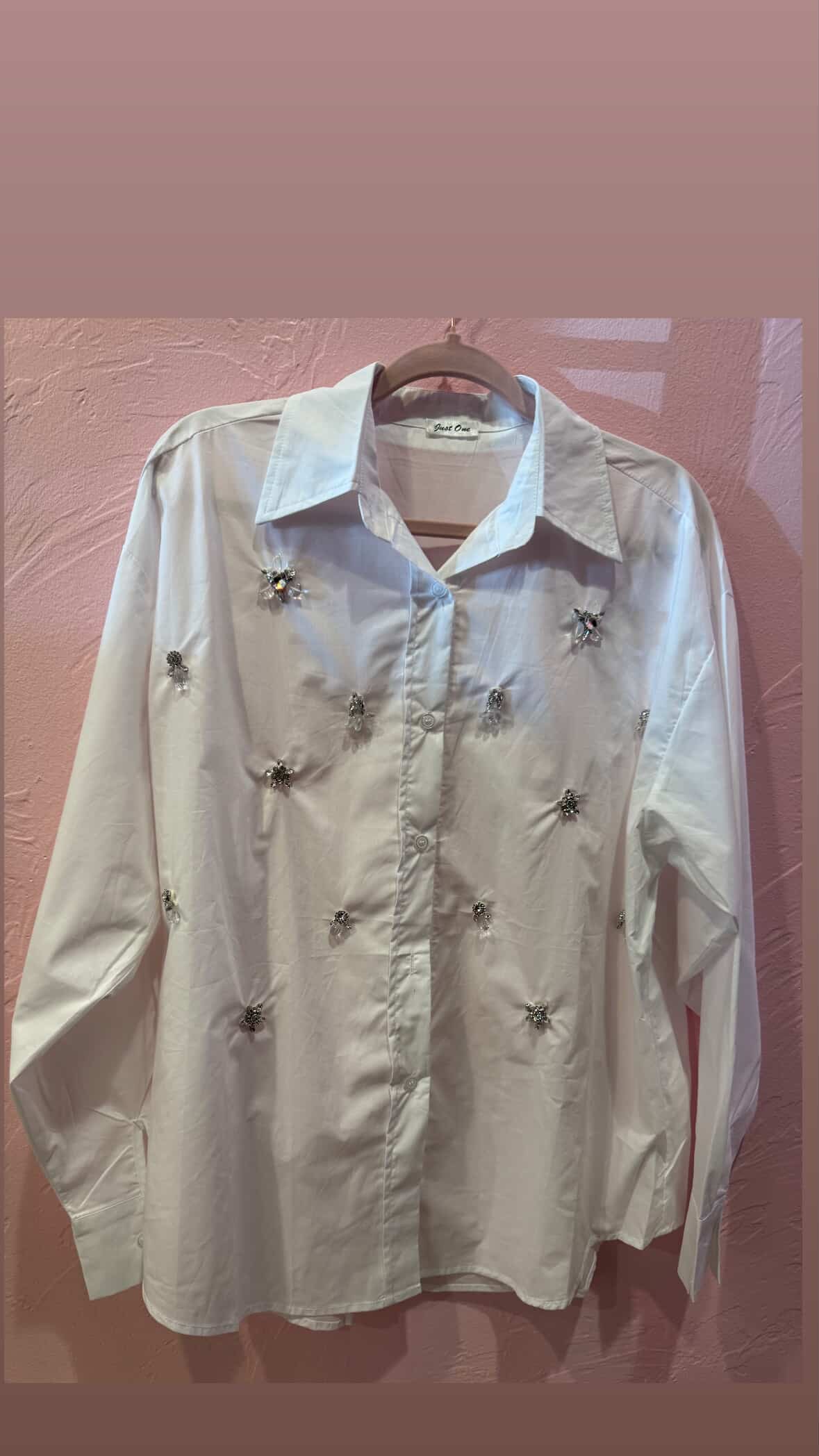 White button-down blouse embellished with crystal jewel accents across the front, displayed on hanger against a pink wall at Milo & Lily Boutique.