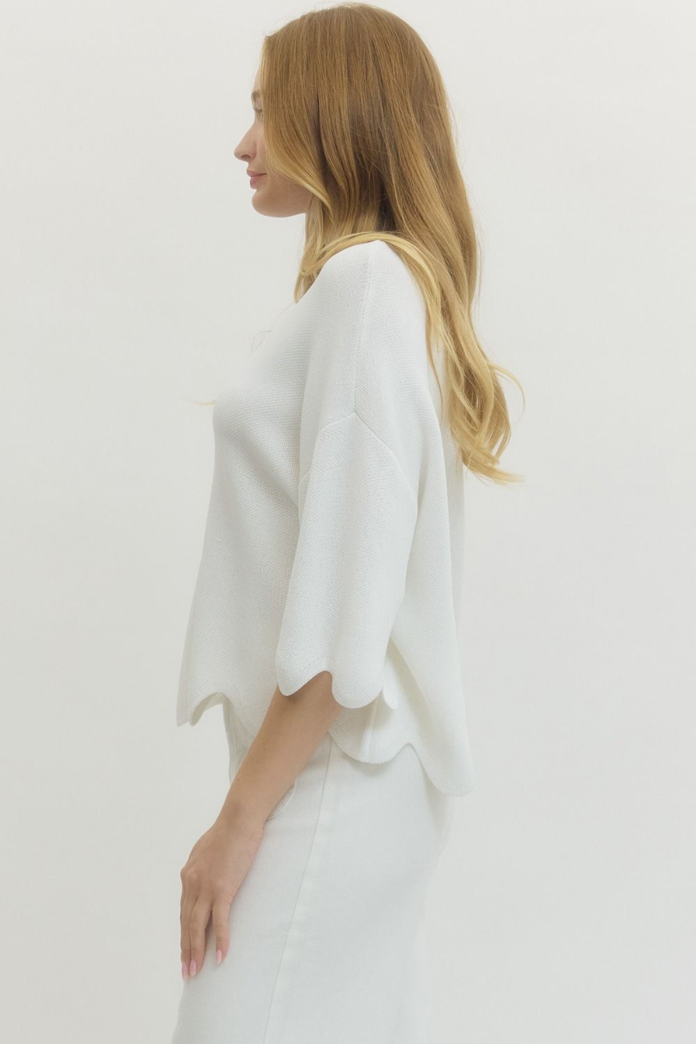 Side view of white lightweight knit top featuring scalloped hem and elbow length sleeves