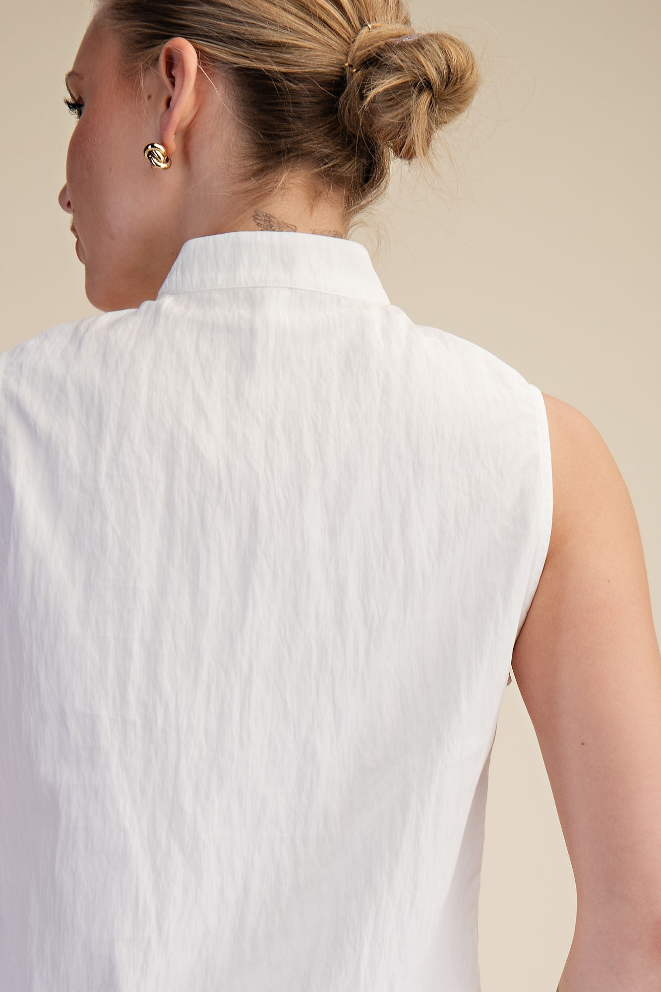 Woman wearing a white sleeveless top against a beige background