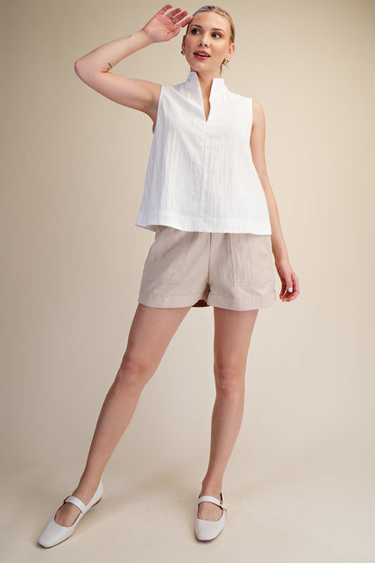 Woman wearing a white sleeveless top and beige shorts on a beige background