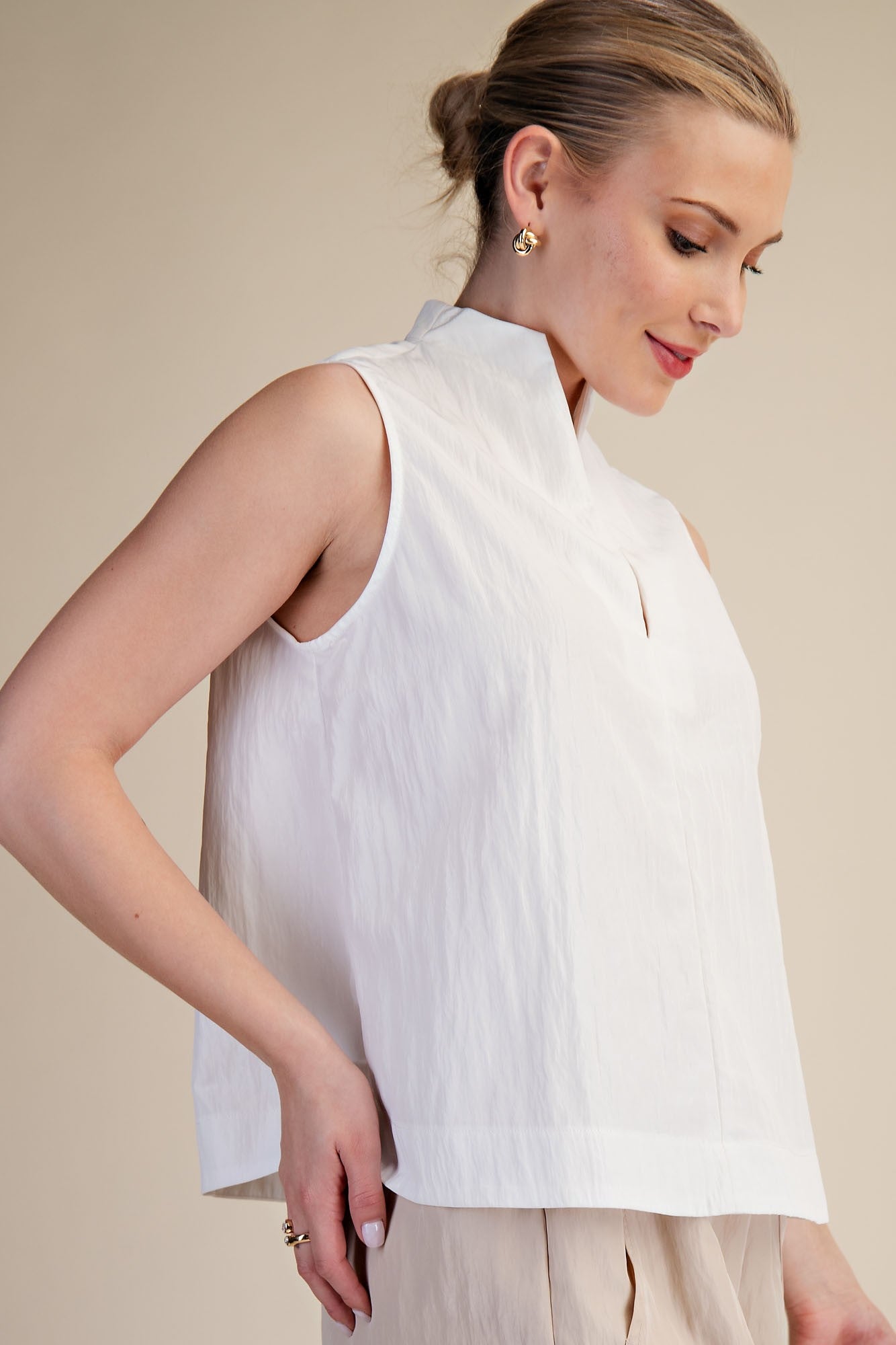 Woman wearing a white sleeveless top against a beige background
